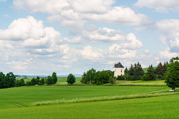 Traditional windmill among green fields under blue sky with white clouds in Saxony near Dresden, Germany. Scenic rural landscape, summer countryside, travel destination.