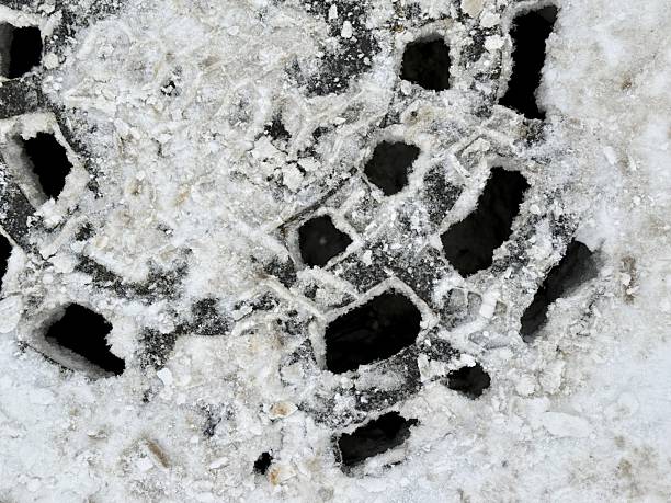 Snow Covered Manhole On Asphalt Road Surrounded By Slush And Ice, Metal Grate Pattern Exposed With Subtle Rust And Wet Patches, Urban Roadside Atmosphere Suggesting Inspection.