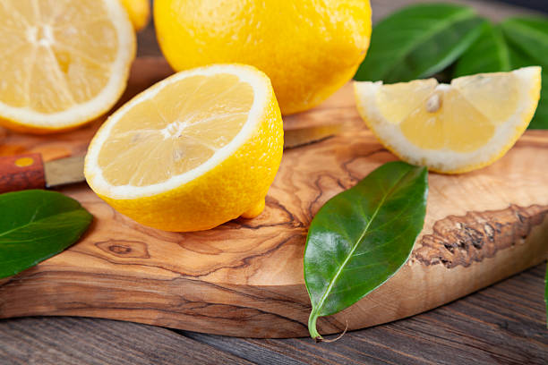 Fresh and ripe lemons with leaves on olive cutting board on brown rustic wooden table.