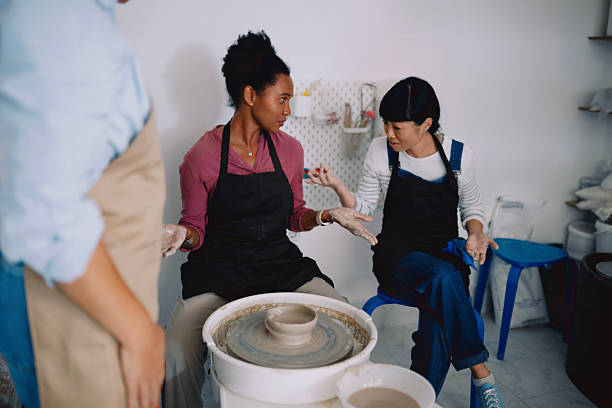 Two women collaborating in a pottery workshop, engaged in crafting and handling ceramic pieces. Surrounded by clay, tools, and handmade pottery, they are focused on their creative work in a warm and artistic environment. The image reflects craftsmanship, teamwork, creativity, and the spirit of small artisanal businesses.