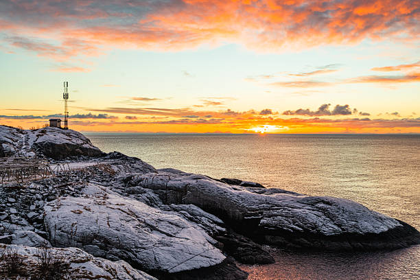 Rocky snow-covered coastline with a communication tower at sunrise or sunset over the sea