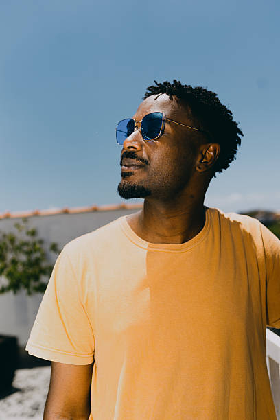 Young man wearing sunglasses standing outdoors in sunlight.