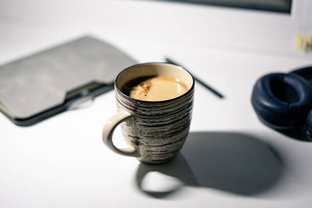 A striped ceramic cup sits on a wooden surface surrounded by coffee beans and spices
