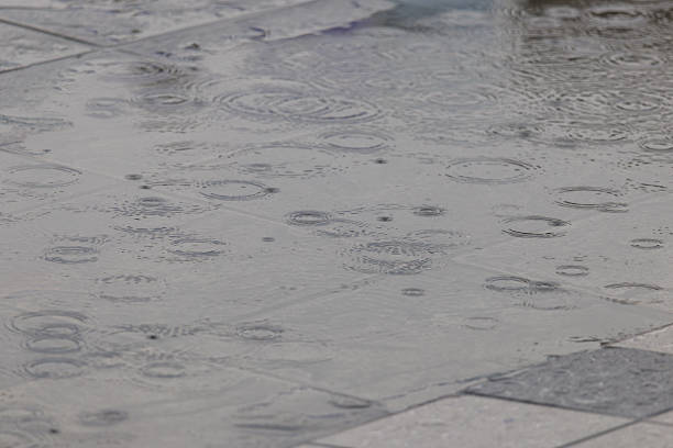 An urban scene reflected in a rain puddle on wet ground, with textured pavement and scattered droplets. Abstract city reflection with a gritty, atmospheric mood.