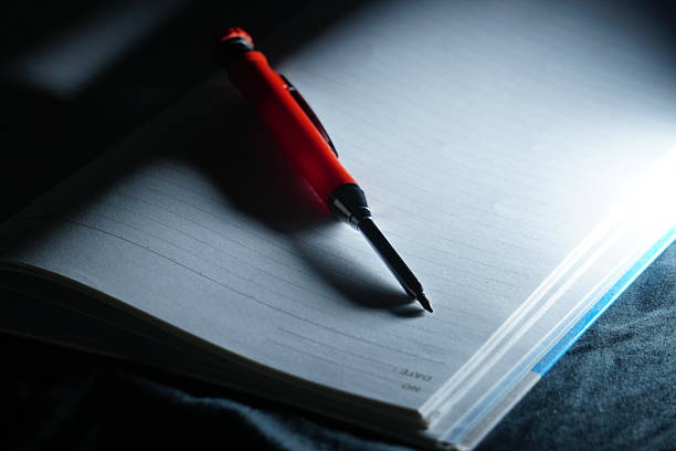 A red mechanical pencil rests on a lined notebook under a cool, blue-tinted light, creating a modern and calm atmosphere for late-night productivity.