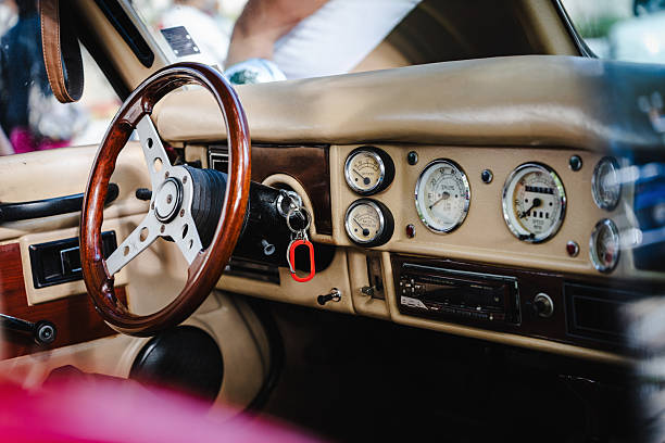 Close up of a classic car cockpit featuring retro steering wheel, wooden dashboard, chrome gear knob, and leather seats showcasing mid-century automotive elegance.