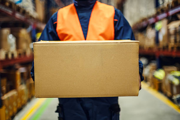 Portrait of handsome young man holding a box in his hands. Delivery man on yellow background