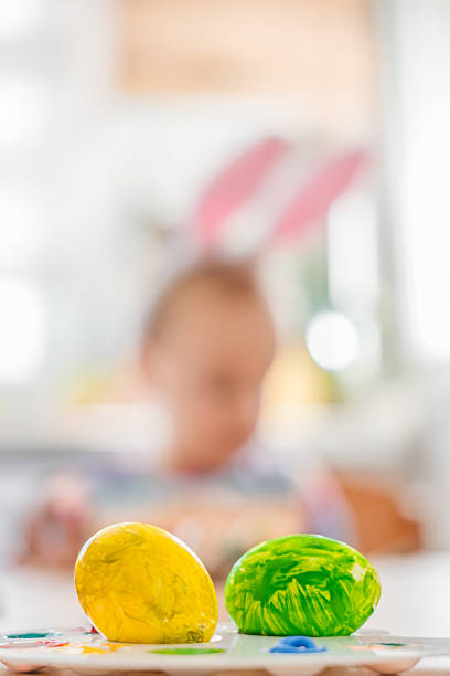 Colorful Easter yellow and green eggs in focus with blurred child in bunny ears background. holiday celebration and spring family tradition. High quality photo