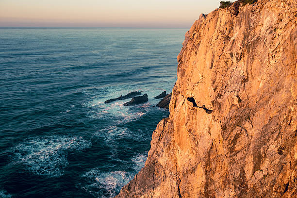 A rocky outcrop at Marinha Beach, Portugal, silhouetted against the soft light of a cloudy sky. Waves gently lap at the shore, creating a serene coastal scene.