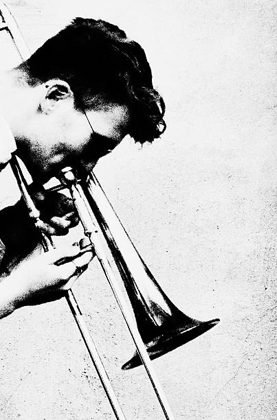 Close-up side profile of a male musician playing trombone against a minimal background, emphasizing texture, contrast and the introspective atmosphere of live performance.