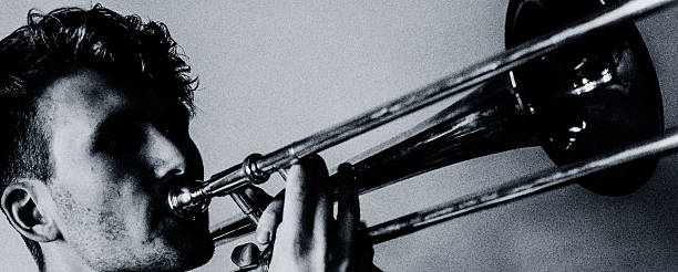 Dramatic black and white portrait of a male brass musician captured in intense concentration, emphasizing texture, shadow and the physicality of live music.