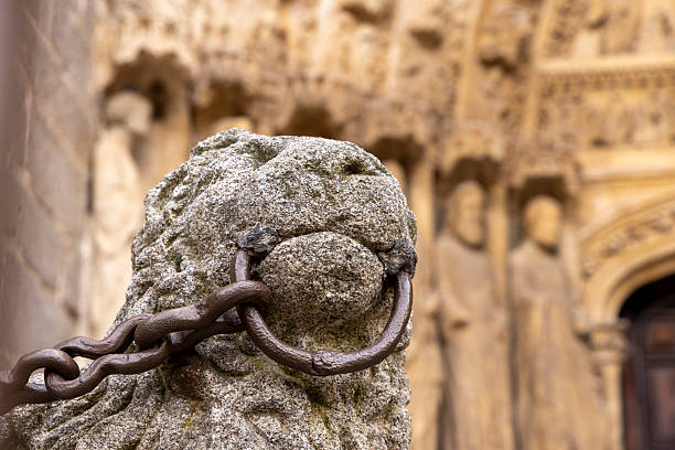 A stone lion with a chain around its neck is standing in front of a building. The lion appears to be looking at the camera, and the chain around its neck gives it a sense of captivity