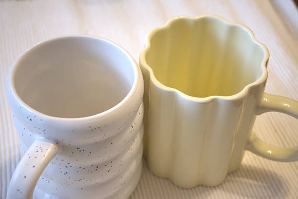 Two wavy shaped mugs placed next to each other on table, symbolizing comparison, partnership, and balance in everyday domestic life. High value concept of relationships, harmony, and decision making.