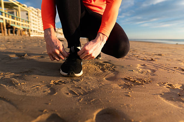 Person tying running shoe laces on sandy beach preparing for a workout