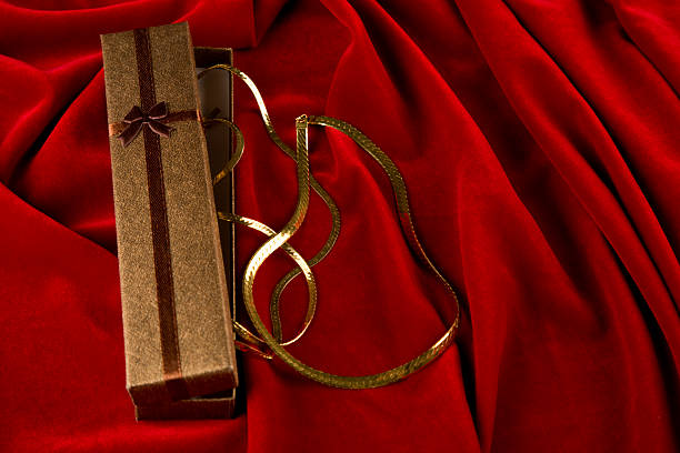 Elegant gift box with gold necklace and copy space on red velvet background