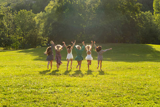 Group of young women running barefoot through grass on a sunny summer evening