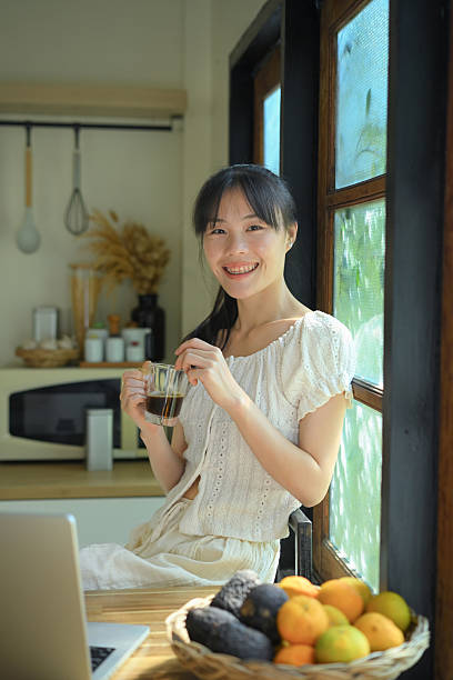 Young woman holding coffee and looking at camera in kitchen.