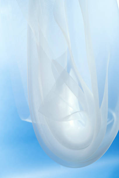 White silk fabric floats gently in the air, creating soft shapes against a blue background. The textile moves slowly, adding a sense of lightness to the space.
