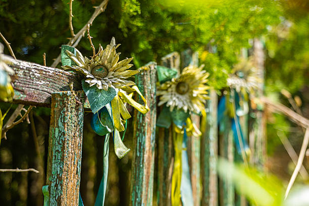 A close-up of a rustic wooden fence with peeling green paint, beautifully decorated with handmade fabric flowers and colorful ribbons. The scene is set in a sunny garden with a lush green background, creating a cheerful and bohemian atmosphere. This image perfectly captures the spirit of a summer festival, folk art, or a charming DIY garden project.