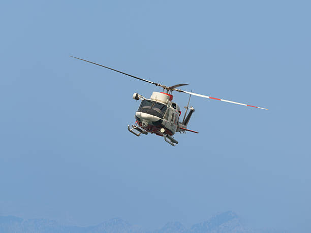 Turkish Coast Guard search and rescue helicopter performs flight over Antalya, Turkey. Front angle view shows aircraft in motion against clear sky and mountain silhouette.
