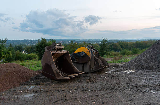 Krakow, Poland – September 13, 2025: Two massive excavator buckets rest on wet soil at a construction area overlooking green hills. The metal attachments lie near piles of aggregate after rainfall, highlighting industrial equipment used in large scale building projects.