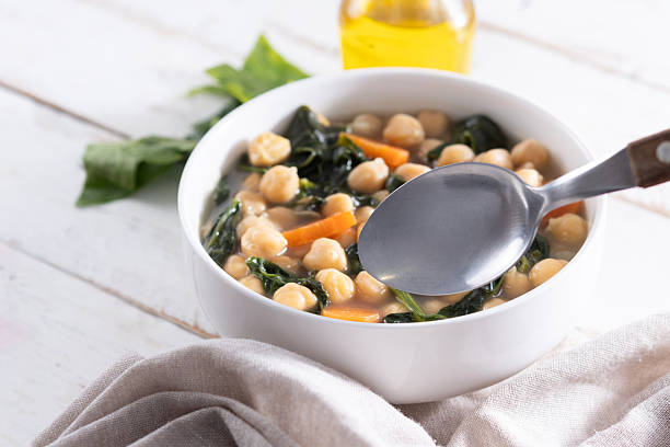 Homemade chickpea and spinach soup with sliced carrots served in a white bowl on wooden table