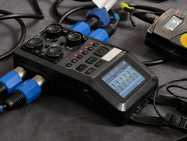 A close-up view of a portable digital audio recorder with XLR inputs, knobs, buttons, and a screen showing audio levels and recording status