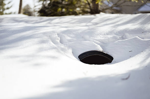 Drain pipe opening submerged in deep snow with winter light and shadows