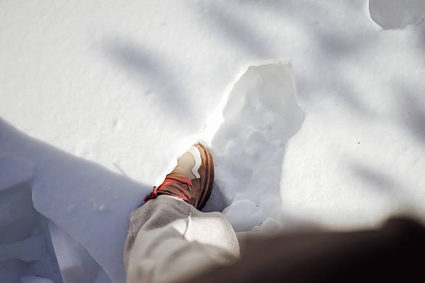 Person's boot stepping into deep snow on a winter day creating a new path