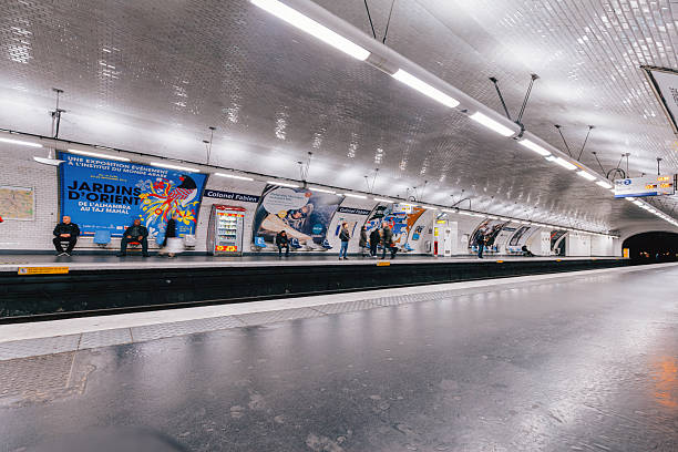 Paris, France - Wide angle editorial view of Colonel Fabien Paris Metro platform showing commuters waiting for train, classic white tiled tunnel design, advertising posters, underground railway tracks and urban public transportation atmosphere inside Paris subway system