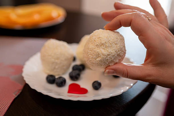 Woman Hand Taking Homemade Coconut Ball Cake from White Plate with Blueberries and Red Heart Decor