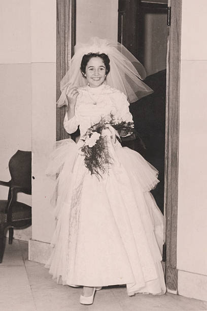 A woman in a wedding dress is standing in front of a window. Scene is elegant and romantic