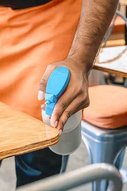 Hand spraying disinfectant on wooden table in restaurant, close-up of worker sanitizing surface to prevent germs, bacteria and ensure public health and foodservice safety