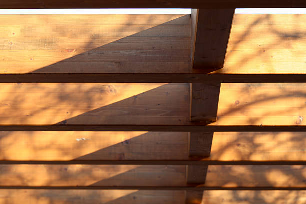 Abstract geometric patterns created by sunlight and tree shadows falling across horizontal wooden beams of an outdoor structure
