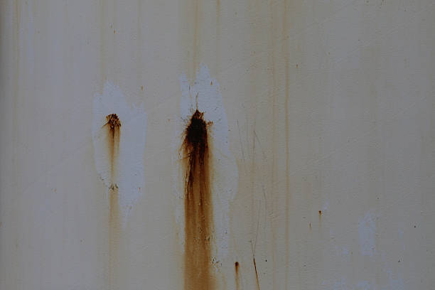 White painted wall with rust stains and streaks from water exposure. Chipped paint and corrosion highlight aging and environmental wear.