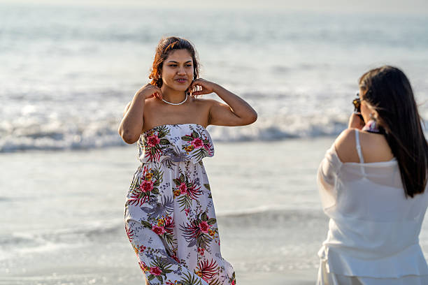 Young woman posing on a beach while her friend takes her picture, capturing moments during sunset vacation