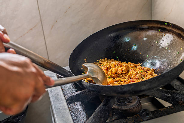 Chef's hands stirring mixed ingredients in a hot wok, preparing delicious chinese-peruvian fusion chaufa rice