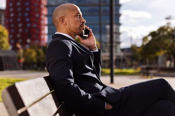 Confident businessman in a suit talks on his phone while seated on a bench in the city
