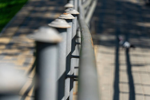 Rusty gray fence posts line a sun-drenched walkway in a peaceful park setting, where gentle shadows play across the ground, creating a serene atmosphere for visitors.