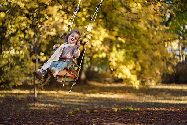 Child playing on outdoor playground. Kids play on school or kindergarten yard. Active kid on colorful swing. Healthy summer activity for children in sunny weather. Little girl swinging.
