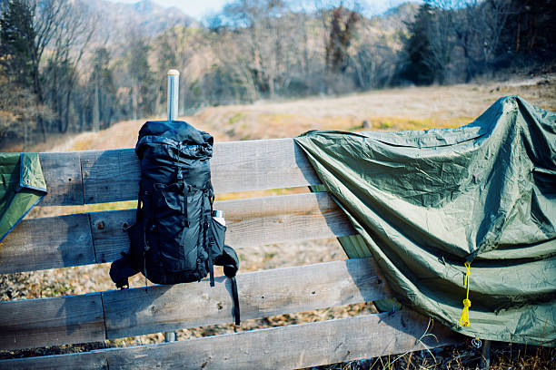 A backpack and camping tarp hanging on a wooden fence in a mountain campsite after packing up. Clear sky and natural landscape create a calm outdoor atmosphere, ideal for camping lifestyle, hiking gear, outdoor adventure, and minimalist travel concepts.