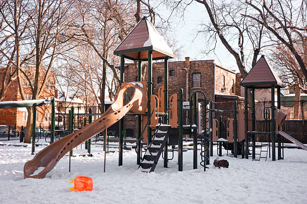 An empty urban playground blanketed in snow featuring a large slide, climbing structures and bare trees, conveying quiet winter stillness and abandoned play space in a residential neighborhood.