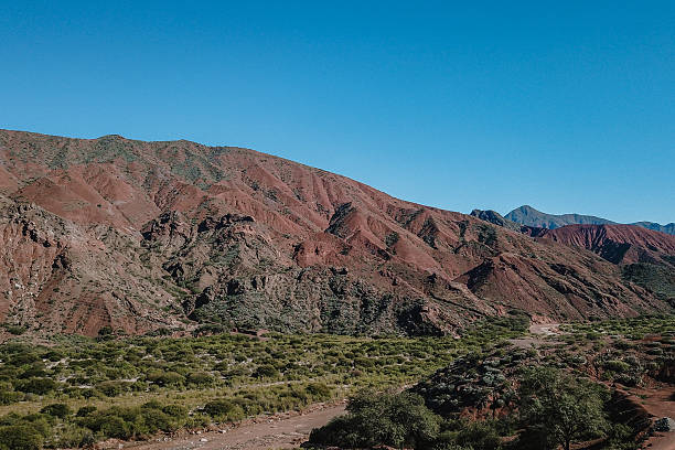 A mountain range with a clear blue sky in the background. The mountains are covered in red rocks