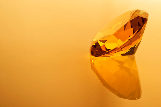 A yellow crystal sits on a flat surface. Light shines on the crystal, creating reflections. The background shows a simple color, focusing attention on the crystal.