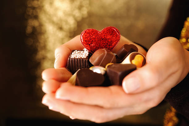 A hand holds a mix of chocolates and a red glitter heart. The scene shows the chocolates ready for sharing or gifting. This moment captures joy and sweetness in a social setting.