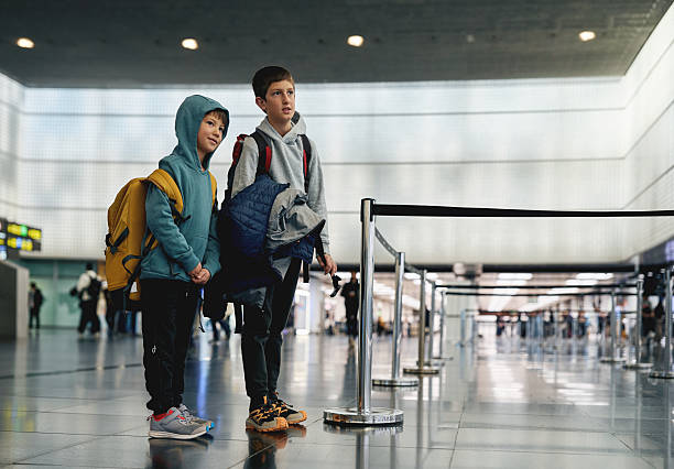 Two children with backpacks waiting in airport terminal near check in queue