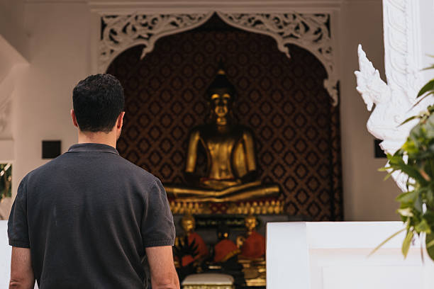 Man from behind looking at a golden Buddha statue inside a Thai temple, contemplating spirituality and respect for culture