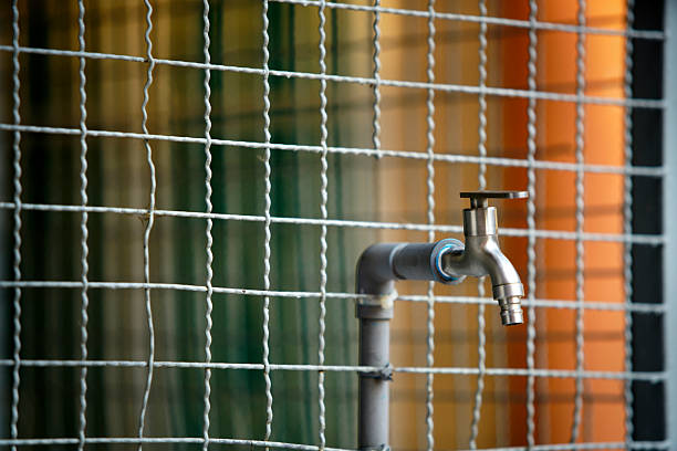 A close-up of a metal faucet installed on a gray pipe, set against a decorative wire mesh and a colorful background. Ideal for plumbing-themed projects.