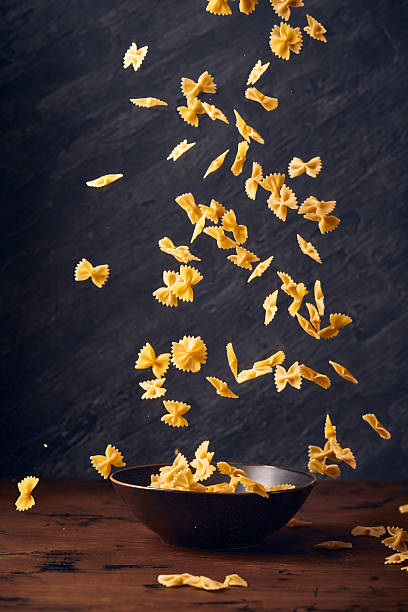 Falling flying and floating in the air raw Farfalle, uncooked Italian Pasta above plate on dark background