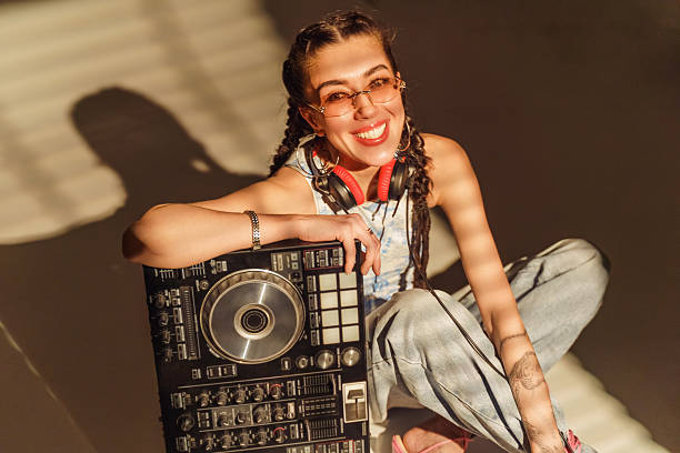 A woman with braided hair smiles while sitting on the floor with DJ equipment and headphones.